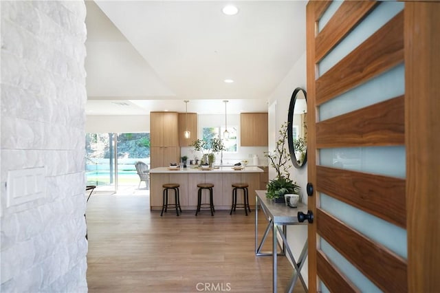 interior space with kitchen peninsula, decorative light fixtures, lofted ceiling, light wood-type flooring, and a kitchen breakfast bar