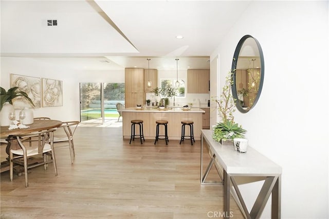 kitchen with a kitchen breakfast bar, kitchen peninsula, pendant lighting, light brown cabinetry, and light hardwood / wood-style flooring