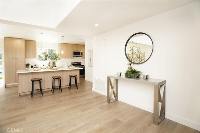 kitchen with a breakfast bar area, stainless steel appliances, hanging light fixtures, kitchen peninsula, and light hardwood / wood-style flooring