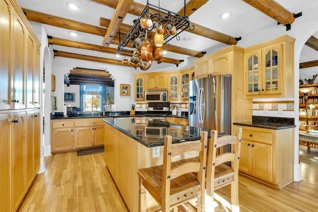 kitchen with a kitchen island, beamed ceiling, dark stone countertops, and appliances with stainless steel finishes