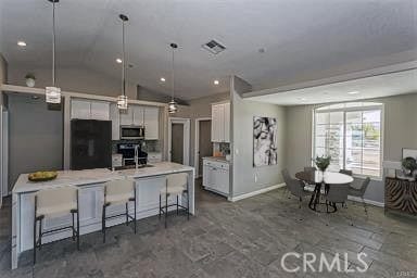 kitchen with decorative light fixtures, white cabinets, black refrigerator, a center island with sink, and a breakfast bar