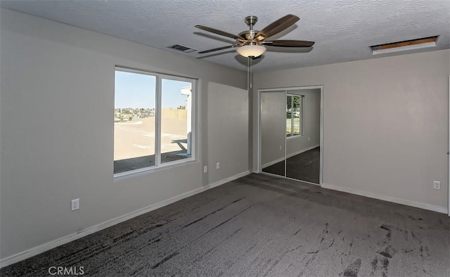 empty room with a textured ceiling, ceiling fan, and dark carpet