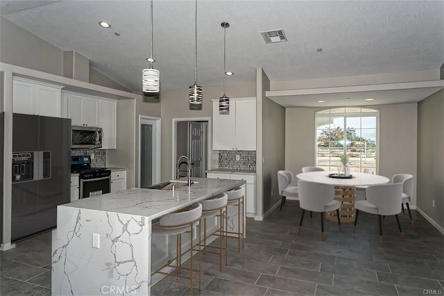 kitchen featuring a center island with sink, black fridge with ice dispenser, stove, and white cabinetry