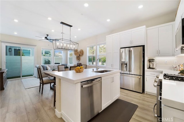 kitchen with sink, stainless steel appliances, an island with sink, white cabinets, and decorative light fixtures