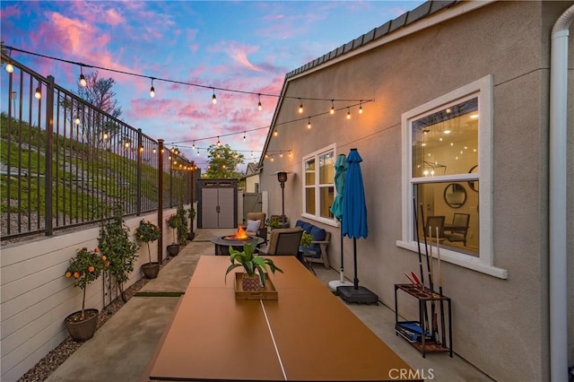 patio terrace at dusk featuring a fire pit and a storage unit