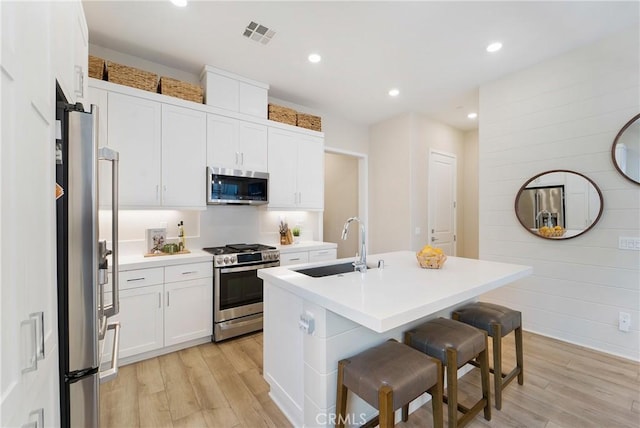 kitchen with white cabinets, a kitchen breakfast bar, a kitchen island with sink, light hardwood / wood-style floors, and stainless steel appliances