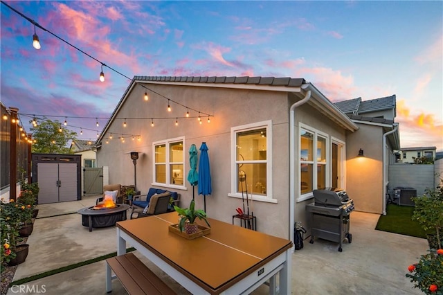 back house at dusk featuring central AC, a patio, a shed, and a fire pit