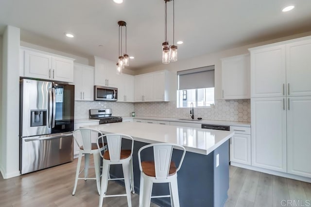 kitchen featuring appliances with stainless steel finishes, pendant lighting, a kitchen island, white cabinets, and sink