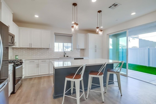 kitchen featuring sink, white cabinetry, a center island, hanging light fixtures, and appliances with stainless steel finishes