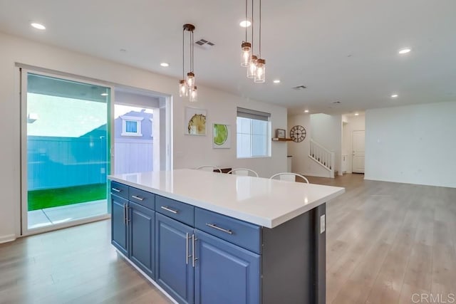 kitchen with light hardwood / wood-style flooring, a center island, blue cabinets, and decorative light fixtures