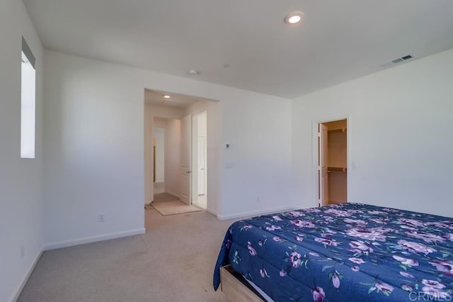 bedroom with a walk in closet, light colored carpet, and a closet