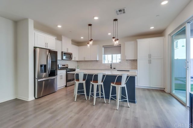 kitchen featuring stainless steel appliances, white cabinetry, light wood-type flooring, and a kitchen island