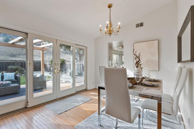 dining room with vaulted ceiling, a notable chandelier, light wood-type flooring, and french doors