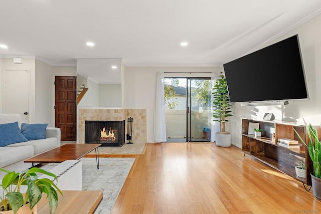 living room with light wood-type flooring, a tile fireplace, and crown molding