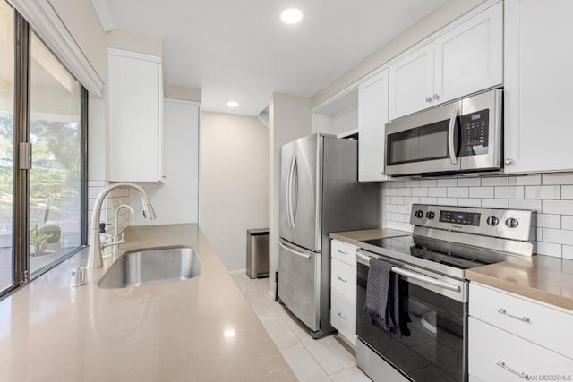 kitchen with stainless steel appliances, light tile patterned floors, decorative backsplash, white cabinets, and sink