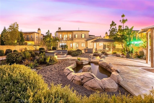 back house at dusk featuring a gazebo, an outdoor fire pit, a patio area, and a balcony