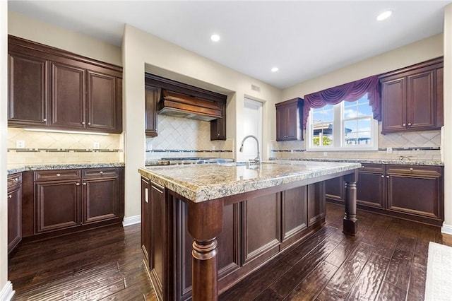 kitchen with light stone countertops, dark wood-type flooring, sink, and a center island with sink