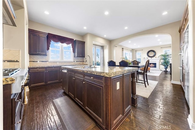 kitchen with sink, backsplash, light stone countertops, a center island with sink, and dark hardwood / wood-style flooring