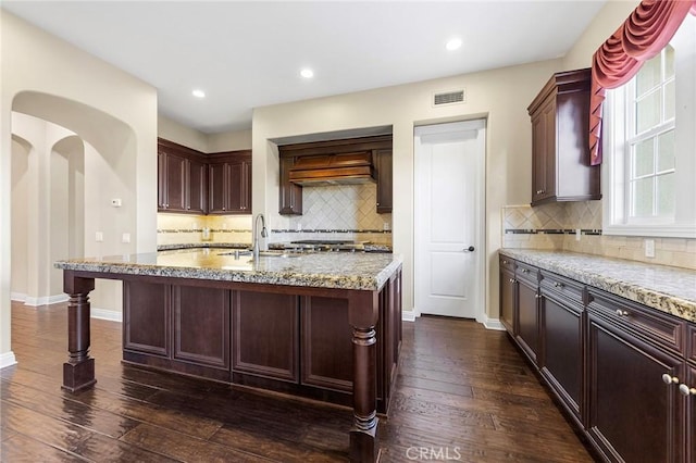 kitchen with sink, a kitchen bar, dark hardwood / wood-style floors, an island with sink, and light stone countertops