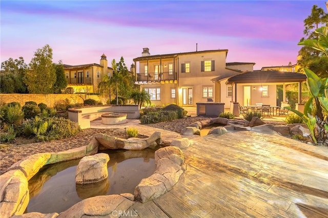 back house at dusk with a fire pit, a balcony, a jacuzzi, and a patio area