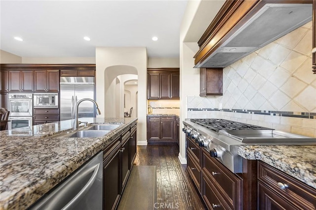 kitchen featuring sink, built in appliances, custom range hood, light stone countertops, and dark hardwood / wood-style flooring