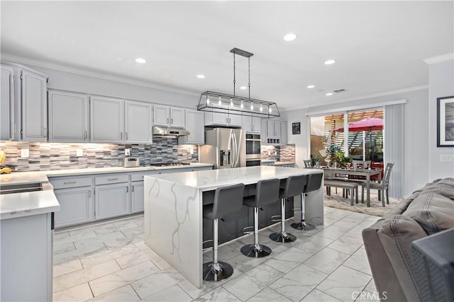 kitchen featuring appliances with stainless steel finishes, hanging light fixtures, a center island, a kitchen bar, and tasteful backsplash