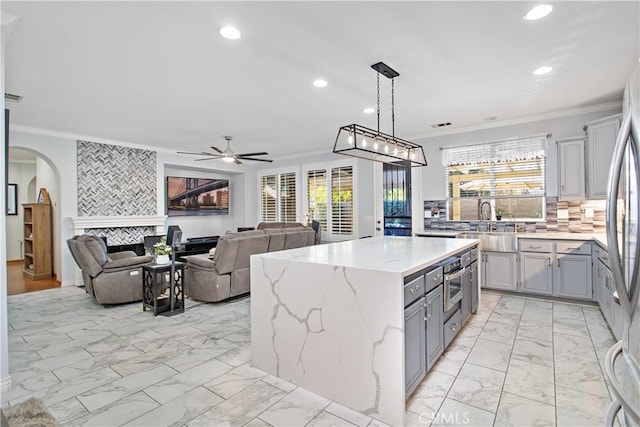 kitchen with hanging light fixtures, a kitchen island, backsplash, a fireplace, and ornamental molding