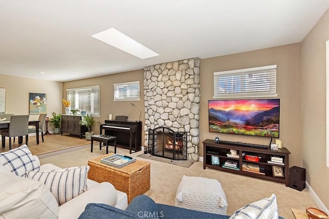 living room with a skylight, light carpet, and a stone fireplace