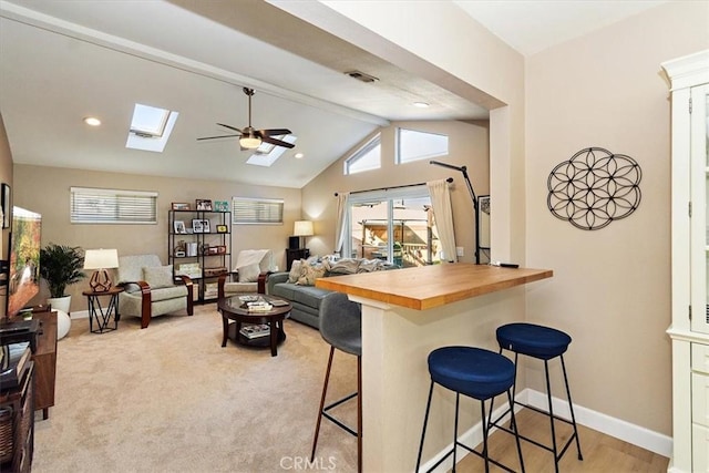 kitchen featuring a kitchen bar, ceiling fan, kitchen peninsula, butcher block countertops, and lofted ceiling with beams