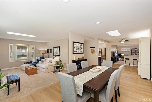 dining room with a skylight, ceiling fan, and light hardwood / wood-style floors