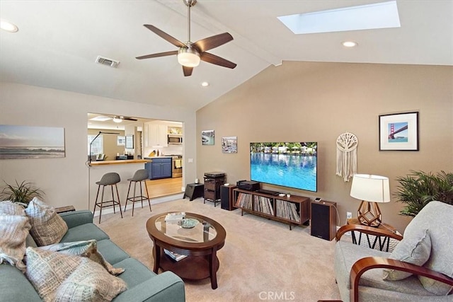 carpeted living room with ceiling fan and vaulted ceiling with skylight