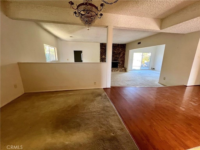 empty room with a fireplace, a textured ceiling, hardwood / wood-style flooring, and a chandelier