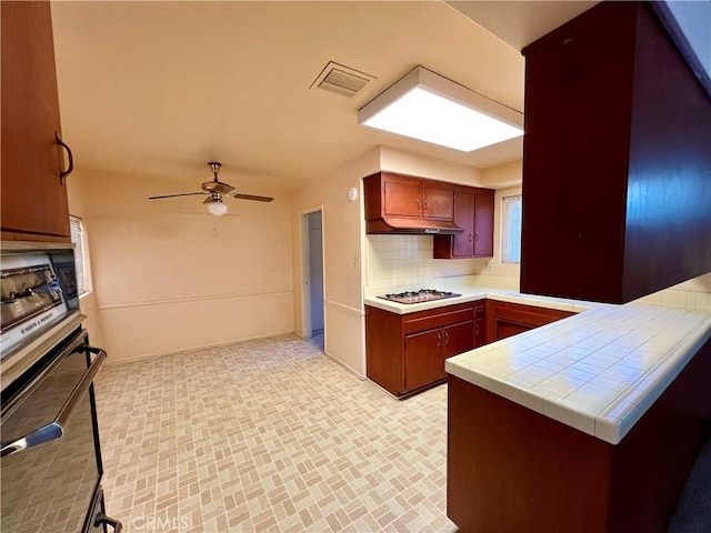 kitchen featuring tile counters, appliances with stainless steel finishes, kitchen peninsula, ceiling fan, and tasteful backsplash