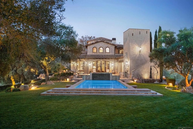 back house at dusk featuring a yard and a patio area