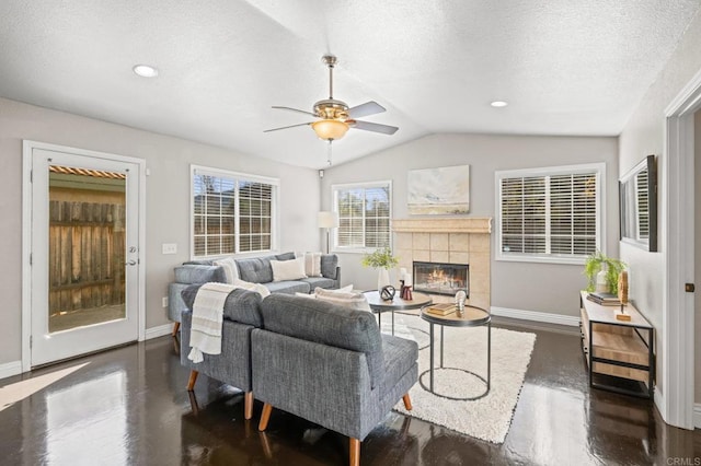 living room featuring a tile fireplace, a textured ceiling, ceiling fan, and vaulted ceiling