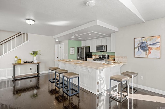 kitchen with kitchen peninsula, a breakfast bar, dark hardwood / wood-style flooring, white cabinets, and appliances with stainless steel finishes