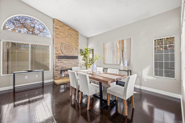 dining area featuring high vaulted ceiling, dark hardwood / wood-style flooring, and a stone fireplace