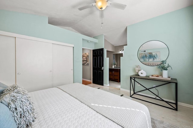 bedroom with vaulted ceiling, a closet, connected bathroom, light wood-type flooring, and ceiling fan