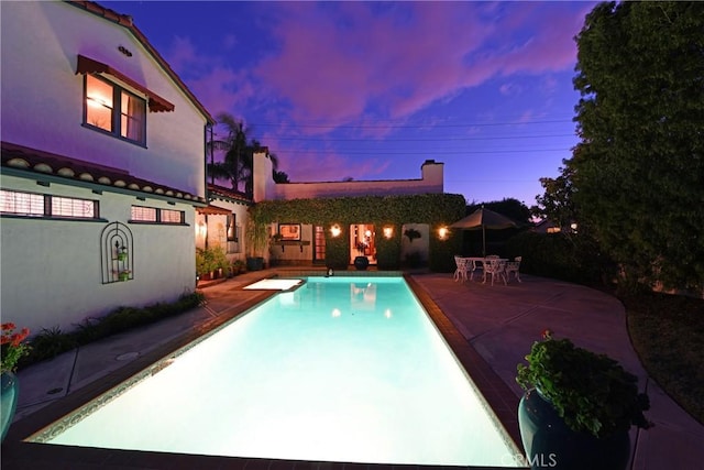 pool at dusk with a patio and an outdoor pool