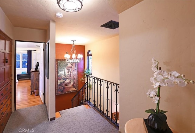 corridor featuring carpet floors, a notable chandelier, an upstairs landing, and visible vents