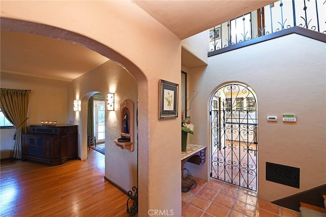 entrance foyer with arched walkways, a textured wall, and wood finished floors