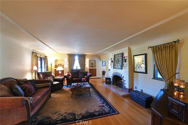 living area featuring arched walkways, a fireplace with raised hearth, and wood finished floors