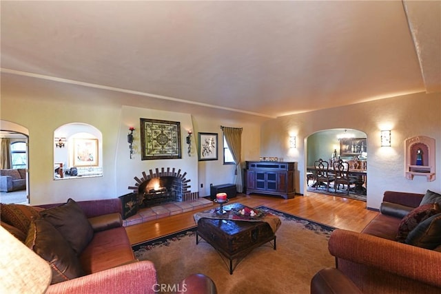 living room with arched walkways, a tiled fireplace, and wood finished floors