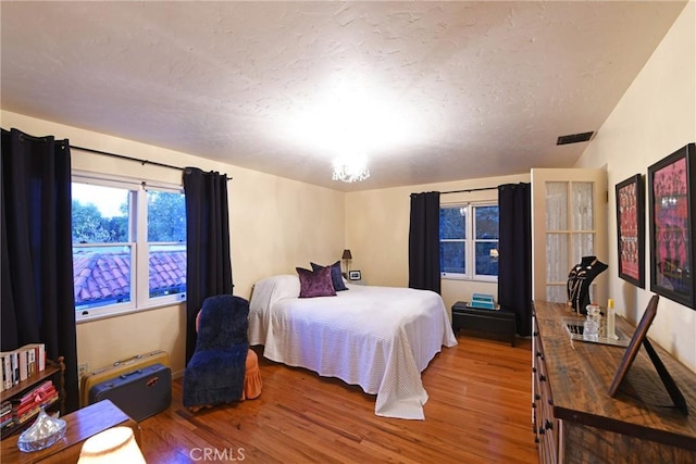 bedroom with a textured ceiling, a chandelier, and wood-type flooring