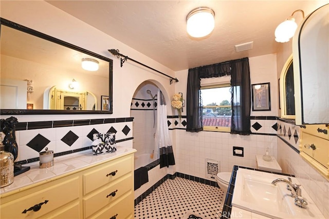 full bath with wainscoting, vanity, toilet, shower / bathtub combination with curtain, and tile walls