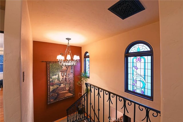 hall featuring visible vents, a chandelier, and an upstairs landing