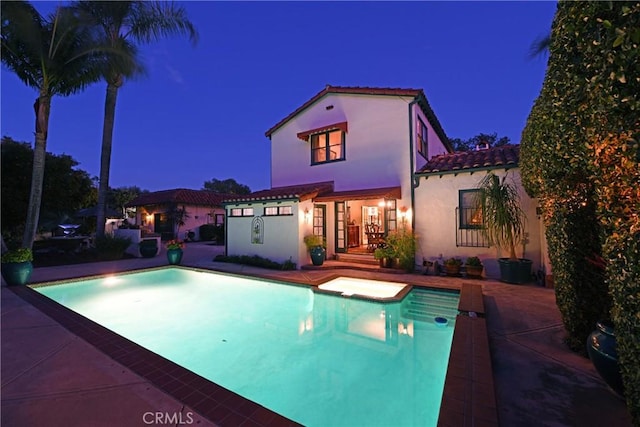 back of house at night featuring a patio area, an outdoor pool, stucco siding, and a tile roof