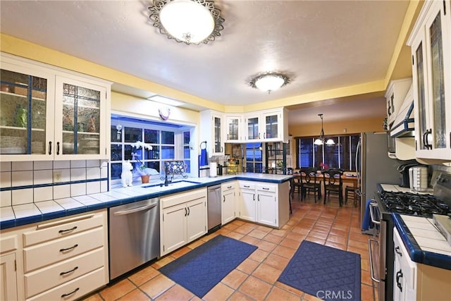 kitchen with tile counters, stainless steel appliances, hanging light fixtures, kitchen peninsula, and white cabinets