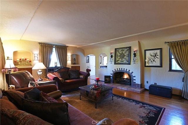 living room with a tiled fireplace, arched walkways, and wood finished floors