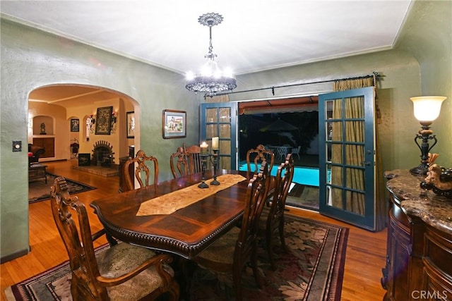 dining room featuring an inviting chandelier, arched walkways, a textured wall, and wood finished floors